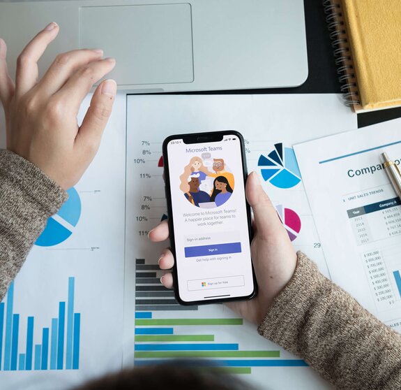 Eine Angestellte lädt auf ihrem Handy die Microsoft Teams App für digitale Zusammenarbeit herunter.