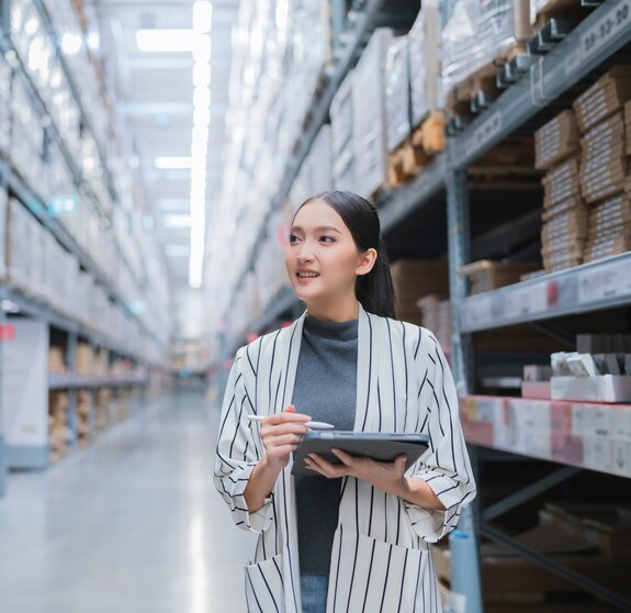 Portrait of asian woman business owner using digital tablet checking amount of stock product inventory on shelf at distribution warehouse factory