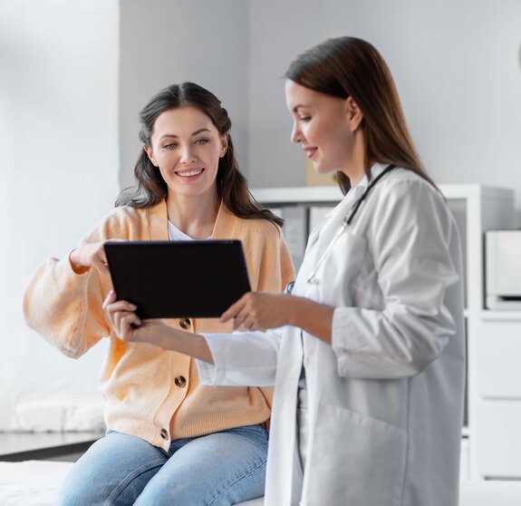 medicine, healthcare and people concept - female doctor with tablet pc computer talking to smiling woman patient at hospital