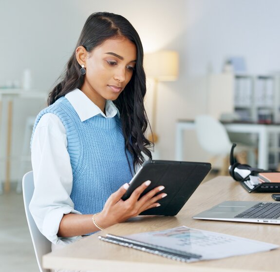 Trendy marketing professional using an online app to network, meet deadlines and stay connected during office hours. Young business woman using her laptop and tablet while working in the office.