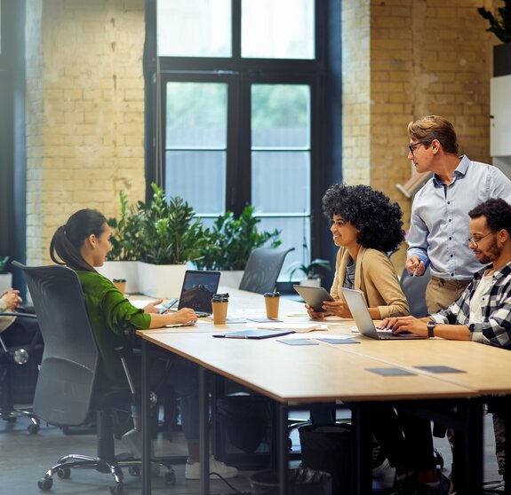 Office life. Group of young multiracial people sitting at the table in coworking space and working together, using modern technologies and discussing project