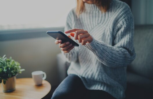 Closeup image of young hipster girl wearing knitted sweater using modern smaertphone device while chilling at home, communication and socail network concept, woman browsing the internet