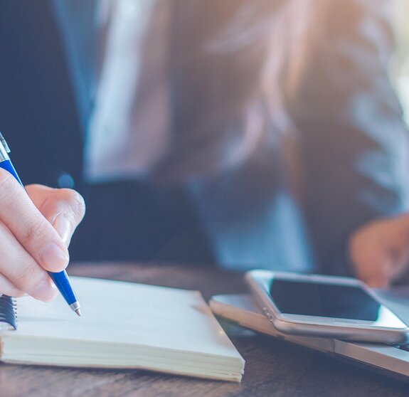 Business woman hand writing on a notepad with a pen and using laptop in the office.