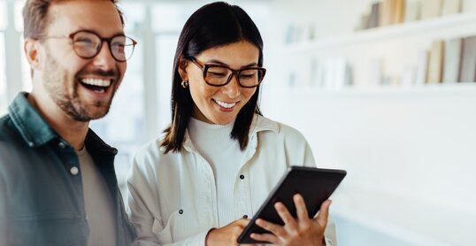 Female designer standing with her colleague and using a tablet