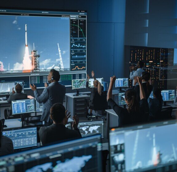 Group of People in Mission Control Center Witness Successful Space Rocket Launch. Flight Control Employees Sit in Front Computer Displays and Monitor the Crewed Mission.