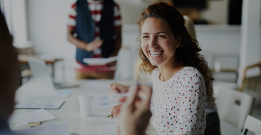 Happy young businesswoman sitting at desk and communicating with her colleagues during a meeting