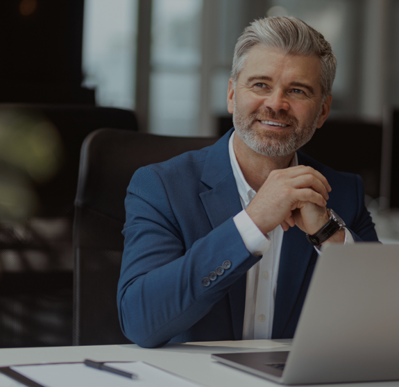 Smiling Mature businessman working on laptop while sitting in modern coworking