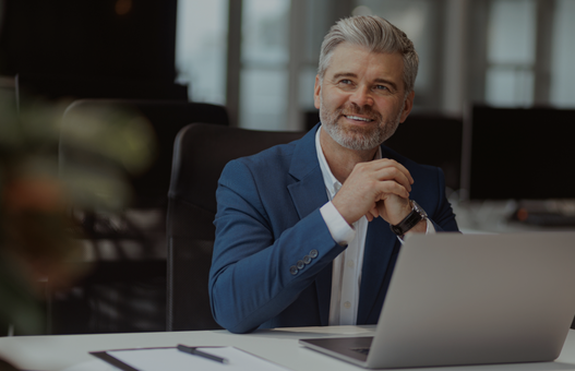 Smiling Mature businessman working on laptop while sitting in modern coworking