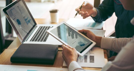 Business partnership coworkers using a tablet to chart company financial statements report and profits work progress and planning in office room.