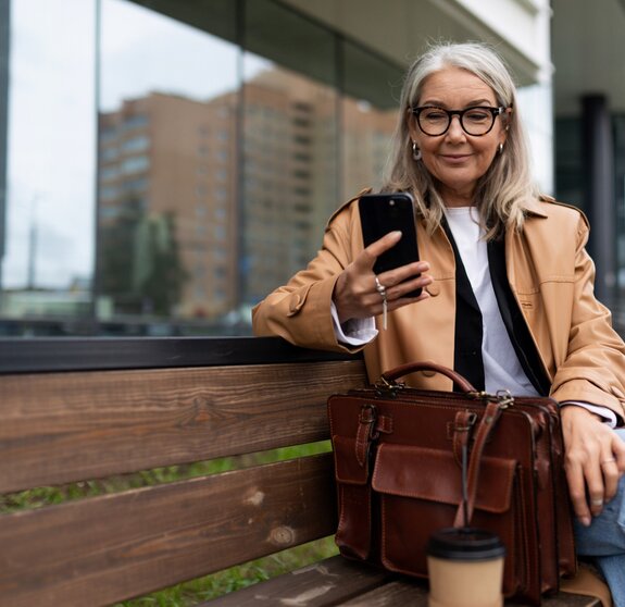 an older woman with a mobile phone sits on a bench outside