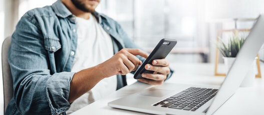 Young man with smartphone in his hands. Modern businessman at sunny office. Freelancer at work.