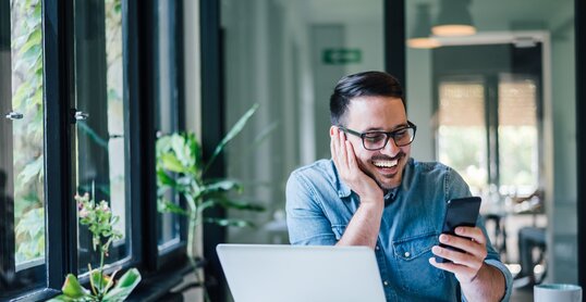 Smiling businessman using phone in home or office. Small business entrepreneur looking at his mobile phone and smiling reading or texting good news.